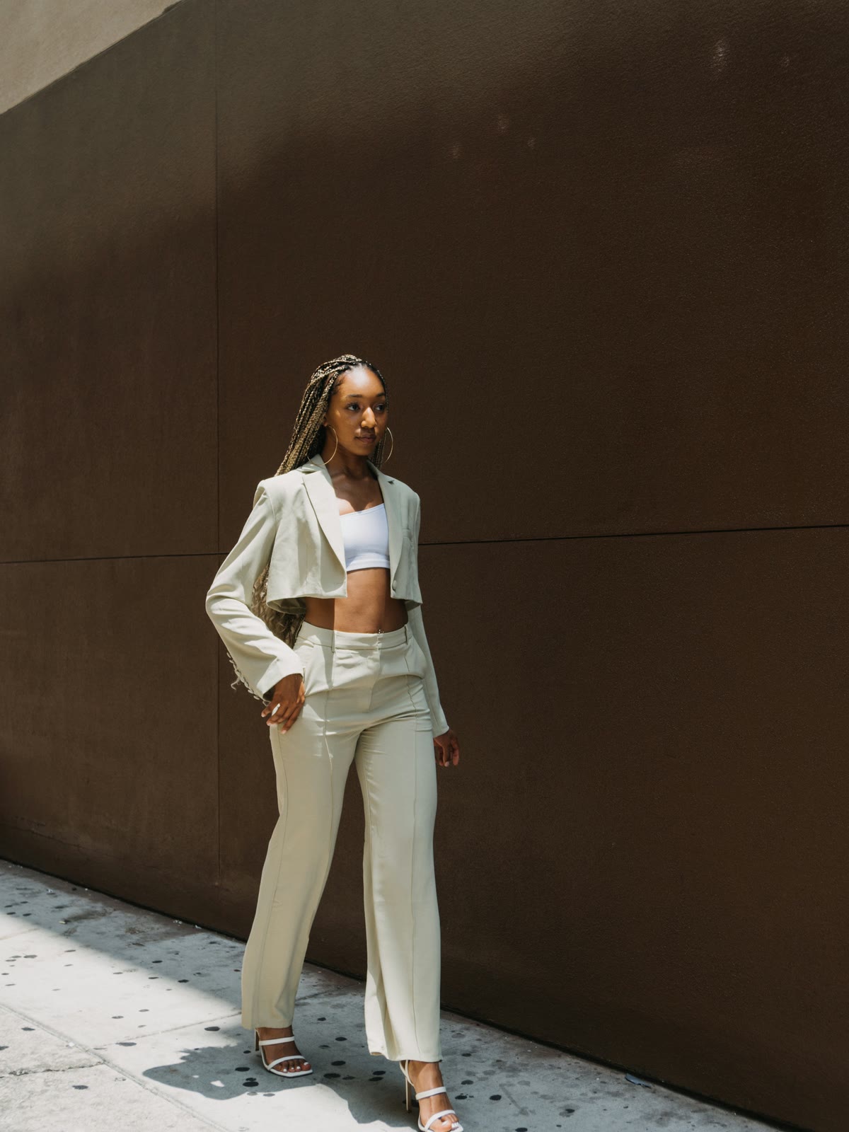 Model in a cream linen top and wide oat trousers against a dark wall